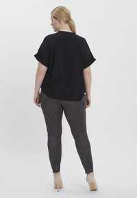 Zwarte, loszittende shirt met opgerolde mouwen en een ronde zoom, gecombineerd met donkergrijze slim-fit broek en beige hoge hakken.