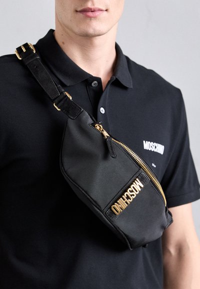 Juodas audinio peties krepšys su auksine užtrauktuku, kuriame išryškintas ryškus "MOSCHINO" logotipas auksine spalva. Jame yra reguliuojama juosta ir glotni tekstūra.