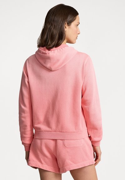 Sweatshirt com capuz rosa feito de um tecido suave, com punhos canelados e um corte descontraído. Apresentado com calções a condizer.