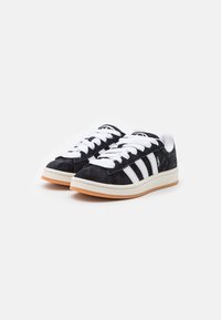 Black suede sneakers with white laces and three white stripes. Features a beige midsole and rubber gum outsole. Classic silhouette design.