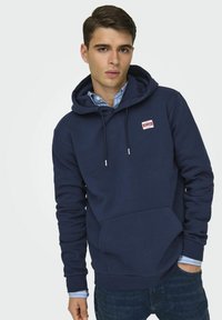 Dunkelblaue Hoodie aus weichem Stoff, mit Kängurutasche, verstellbarem Kordelzug und einem kleinen Logopatch auf der Brust.