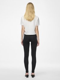 Hvit cropped t-skjorte parret med svarte leggings. T-skjorten har korte ermer, og leggingsene sitter tett og har en glatt tekstur. Svarte hælhæler.