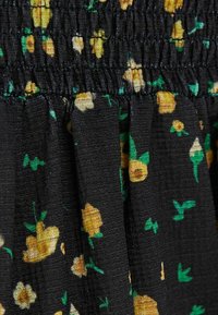 Schwarzer Stoff mit strukturierter Oberfläche, der ein florales Muster aus gelben Blumen und grünen Blättern zeigt, am oberen Rand mit elastischem Detail gerafft.