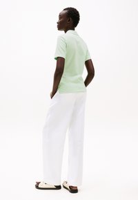 Mintgrønn polo skjorte paret med hvite vide bukser og beige sandaler. Skjorten har kort krage og en avslappet passform.