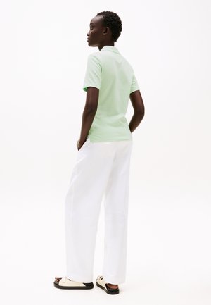 Mintgrønn polo skjorte paret med hvite vide bukser og beige sandaler. Skjorten har kort krage og en avslappet passform.