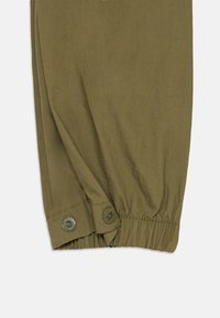 Olivgrüne Hose mit einem gesmokten, elastischen Saum, versehen mit zwei silbernen Metallknöpfen am Knöchel und einem glatten, strukturierten Stoff.