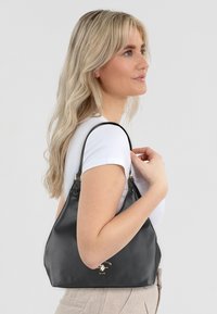 Borsa a spalla in pelle nera con finitura textured, dettagli in hardware dorato e forma arrotondata, portata sulla spalla da un modello.