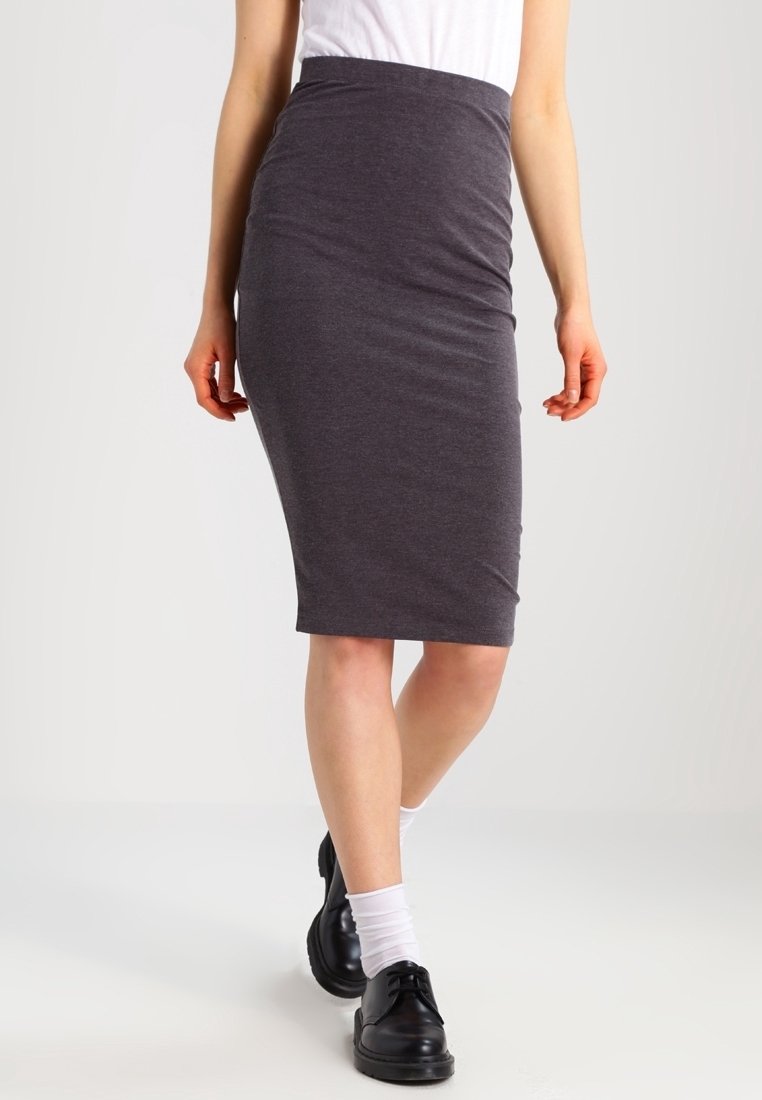 Femme portant une jupe crayon gris foncé jusqu'aux genoux, un haut blanc, des chaussettes blanches et des chaussures noires à lacets marchant vers l'avant.