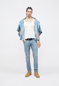 Ανοιχτό μπλε τζιν παντελόνι, λευκό αμάνικο κορμάκι και ανοιχτό μπλε τζιν πουκάμισο περασμένο πάνω από τους ώμους. Καφέ υποδήματα ολοκληρώνουν την καθημερινή εμφάνιση.