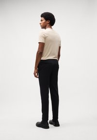 Beige fitted t-shirt, black slim-fit trousers, and black ankle boots. Smooth fabric with minimal detailing, viewed from the back.