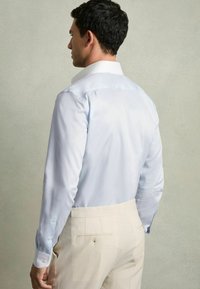 Lichtblauw overhemd met lange mouwen, met knoopmanchetten, gestructureerde kraag, gladde textuur, gecombineerd met beige broeken.