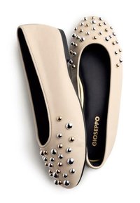 Bailarinas de cuero beige con interior negro, con tachuelas metálicas redondas en plata y oro a lo largo de la parte frontal, y un diseño de punta redondeada.