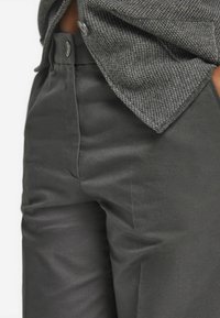 Grau strukturierte Hemd mit Knopfleiste verdeckt teilweise elegante dunkelgraue Hosen. Der Stoff wirkt glatt mit einem leichten Glanz, was die taillierte Passform betont.