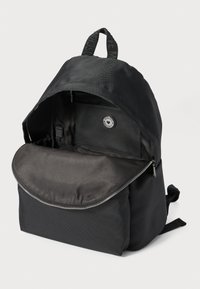 Melnā mugursoma ar atvērtu galveno nodalījumu, kurā redzama iekšējā kabata ar apaļu logotipa detaļu un augšējo rokturi ar drukātu tekstu.