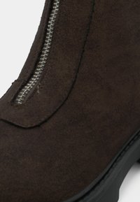 Dark brown suede ankle boot featuring a silver zipper detail along the front seam, with a textured finish and a black rubber sole.