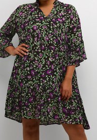 Blumenkleid mit dunklem Hintergrund, das grüne Blätter und lila Blumen zeigt. Es hat einen V-Ausschnitt, Dreiviertelärmel und einen lockeren Schnitt.