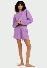 Lila bomullsgymnastiktröja med översized passform, långa ärmar och ribbad textur, i kombination med matchande lätta shorts.