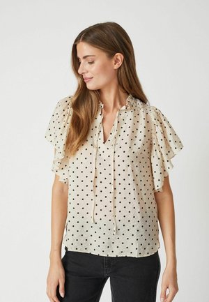 Blusa crema trasparente con pois neri, maniche corte a sbuffo, scollatura arricciata e un dettaglio con fiocco nella parte anteriore. Tessuto liscio e piatto.