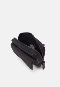 Piccolo astuccio nero con cerniera aperto per mostrare l'interno con un'etichetta del marchio visibile all'interno su uno sfondo bianco semplice.