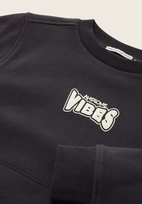 Must must ja orgaanilisest puuvillast, millel on tekstureeritud ribitatud ümar kaelus ja ees valge print "AWESOME VIBES".