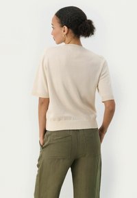 Pull en maille beige à manches courtes avec des poignets et un ourlet côtelés, associé à un pantalon olive vert ample avec des poches arrière et une texture douce.