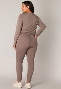 Langsleeve taupe top gecombineerd met aansluitende taupe leggings, met achterzakdetails en zachte, rekbare stof.