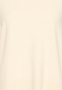Gros plan d'un pull en maille couleur crème montrant la texture et le détail de l'ourlet côtelé.