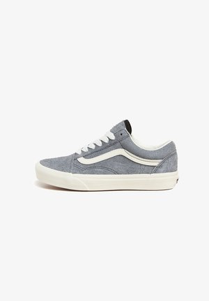 Zapatilla deportiva baja gris con franja lateral blanca, cordones blancos y suela gruesa blanca de goma sobre fondo blanco liso.