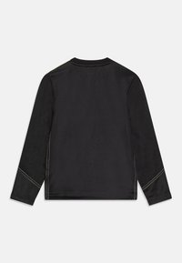 Černá košile s dlouhými rukávy a kontrastním žlutým prošíváním, hladká textura, kulatý výstřih a přizpůsobený střih, zobrazující pouze design na zadní straně.