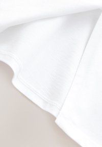Tissu en coton blanc avec une texture lisse, montrant l'ourlet et les détails de couture. Le matériau est léger et légèrement extensible.