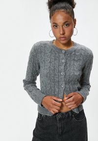 Cardigan gris de punto con un patrón de trenzas, puños y cuello acanalados, con cinco botones en el frontal, corto en longitud.