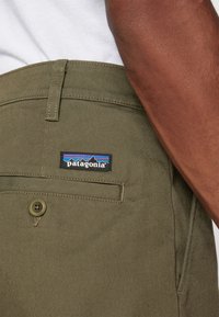 Olive zelene hlače iz bombaža z zadnjim žepom, ki imajo črno oznako Patagonia in detajl z gumbnico.