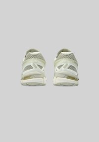 Scarpe da ginnastica di colore chiaro con tomaie in mesh, suole ammortizzate e un design strutturato. Presentano un tallone rinforzato e dettagli con il logo sui lati.