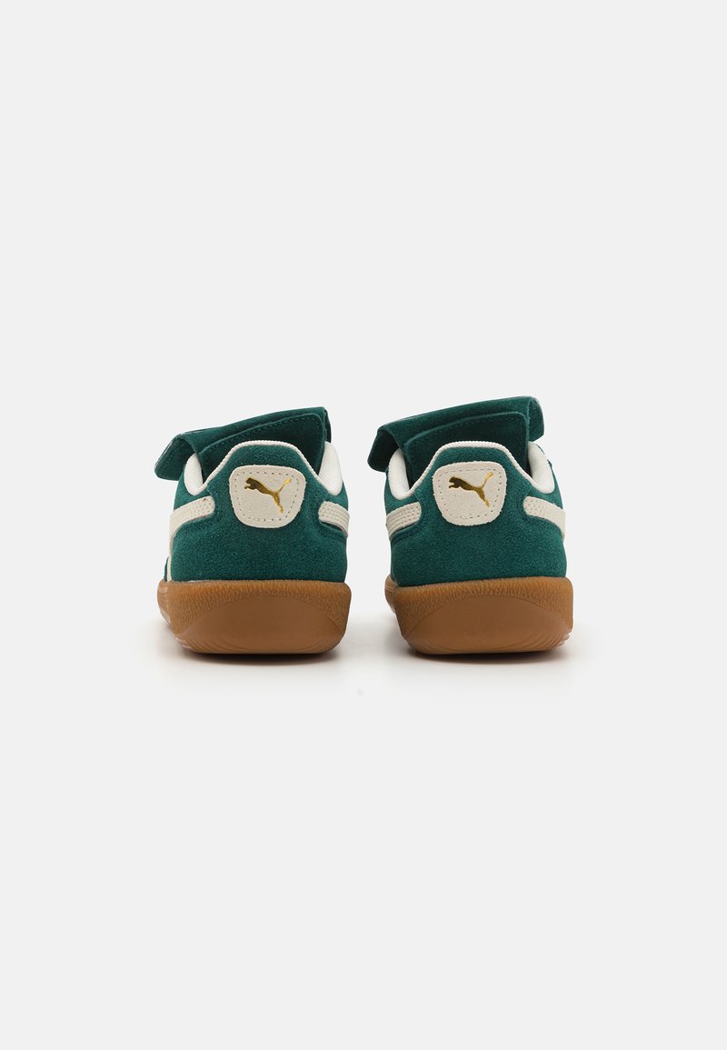 Sneaker in suede verde con suola in gomma marrone, dettagli bianchi e toppa con logo sul retro. Il design include un tallone imbottito per il comfort.