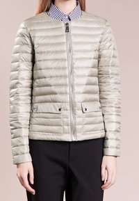 Light gray puffer jacket with a quilted design, front zipper, two pocket flaps, and ribbed cuffs. Features a logo on the left chest.