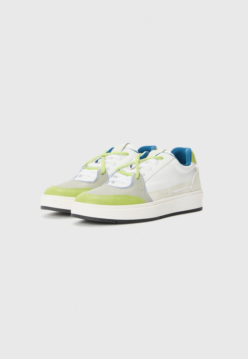 Sneaker con una toma bianca, accenti verde chiaro, interno blu e materiale texture, con una suola spessa e una suola nera a contrasto.