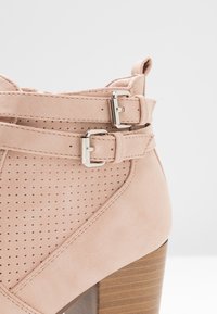 Botte de cheville rose pâle en suède perforé avec deux boucles en argent ajustables et un talon empilé en bois.