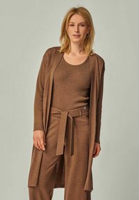 Braun gerippter Strickcardigan über einem passenden Tanktop und einer Hose, mit einem Bindegürtel und offenem Design, das einen geschichteten Look kreiert.