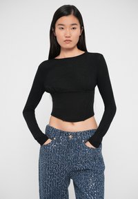 Black long-sleeve cropped top with a round neckline and gathering at the bust, paired with blue textured pants embellished with metallic accents.
