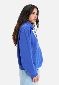 Sudadera azul con cuello alto y cordón, presenta un bolsillo canguro y puños acanalados. Tejido suave y corte relajado.