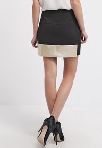 Zwarte minirok met een glanzende gouden onderband, met een aansluitend ontwerp. Draag het met zwarte hoge hakken.
