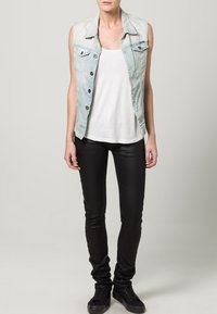 Ljusblåjeans västar utan ärmar med mörka knappar, bärs över en vit linne; matchas med svarta slim-fit byxor och svarta sneakers.