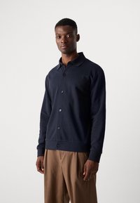 Camisa de botones de manga larga color azul marino con cuello, confeccionada en una tela suave, que presenta un dobladillo recto y detalles de botones en la parte delantera.