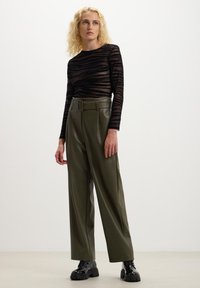 Maglietta a maniche lunghe a righe nere in tessuto trasparente abbinata a pantaloni alta vita in finta pelle verde oliva. Stivaletti neri chunky completano il look.