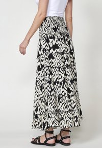 Jupe longue noire et blanche à volants avec un motif abstrait audacieux, fabriquée en tissu léger. Caractérisée par une ceinture froncée et un ourlet à volants.