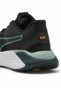 Musta urheilukenkä, jossa on teksturoitu yläosa, turkooseja yksityiskohtia ja valkoinen välikerros, jossa lukee "PROFOAM". Puma-logo kantapäässä.