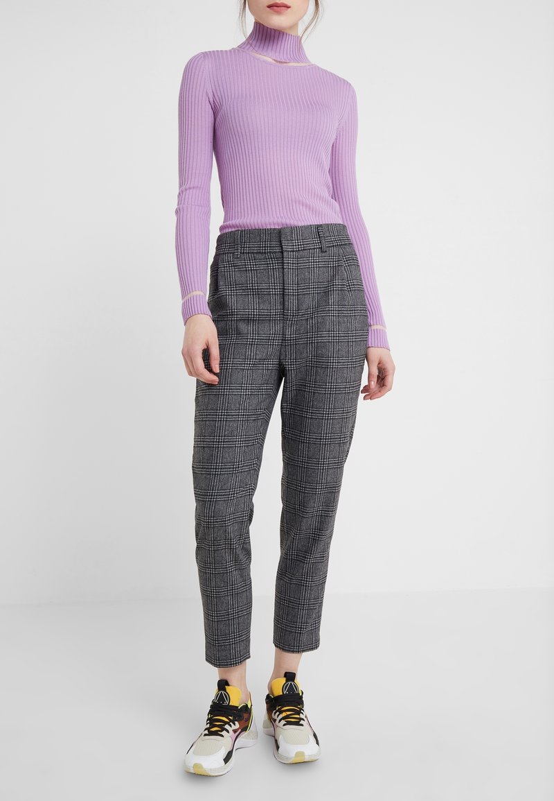 Femme portant un pull côtelé ajusté lavande, un pantalon court taille haute à carreaux gris, et des baskets blanches avec des accents jaunes et noirs.