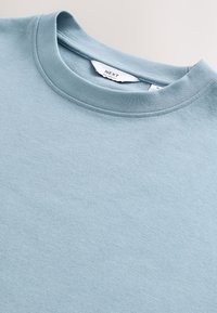 Hellblauer Sweatshirt mit Rundhalsausschnitt, weicher Stoffstruktur und sichtbarem weißen Etikett innen im Kragen.