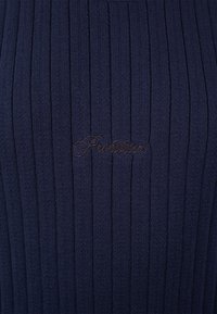Tissu tricoté côtelé bleu foncé avec un texte en écriture cursive brodé subtilement, centré horizontalement.