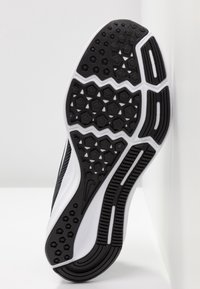 Semelle de chaussure de sport en noir et blanc, présentant un motif hexagonal pour l'adhérence, des surfaces texturées et un contour incurvé de couleur blanche.